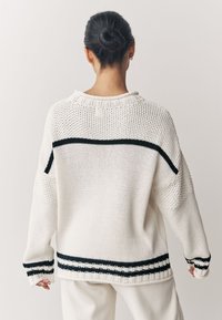 Suéter tejido en color crema con rayas negras en el dobladillo y los hombros. Corte holgado, tela texturizada con puños y escote acanalados.