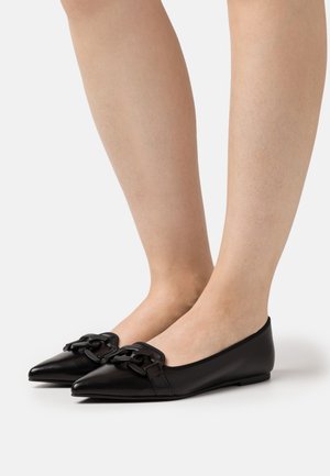 Ballerines en cuir noir avec des bouts pointus et une accentuation de chaîne décorative sur le devant, présentant une texture lisse et un matériel minimal.