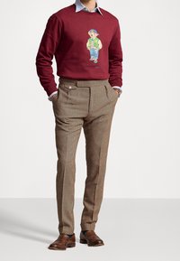 Sudadera burdeos con un gráfico de un oso de dibujos animados, combinada con pantalones cuadrados marrones y zapatos de piel marrones.