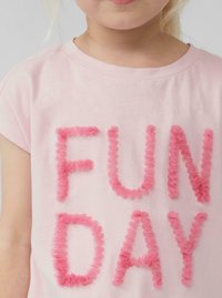 Roze katoenen t-shirt met de tekst "FUN DAY" in textuurrijke, gerimpelde roze stoffen letters. Korte mouwen en een ronde hals.