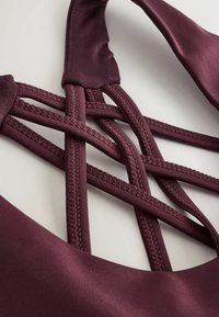 Bordeaux sportbeha met een satijnen afwerking, crisscross bandontwerp en een gladde textuur, met gestikte accenten langs de banden.
