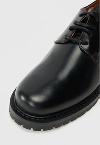 Schwarzer Lederschuh mit runder Zehenform, subtiler Glanz, Schnürdesign, strukturiertem Zunge und einer dicken, robusten Gummisohle.