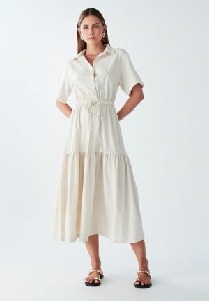 Light beige midi dress with short sleeves, button front, elastic waist, and tiered skirt. Smooth fabric with a subtle texture.