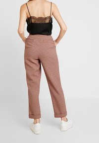 Svart spetstopp med rygg i spets, parat med rutiga, högmidjade byxor i rött och beige, med avslappnad passform och sidofickor. Vita sneakers.