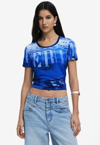Blue graphic t-shirt with bold text design, short sleeves, and a round neckline, paired with light blue high-waisted jeans.
