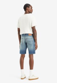 Shorts in denim con un lavaggio azzurro chiaro, vestibilità dritta e orli arrotolati. Abbinati a una t-shirt bianca e calzini bianchi con scarpe da ginnastica.