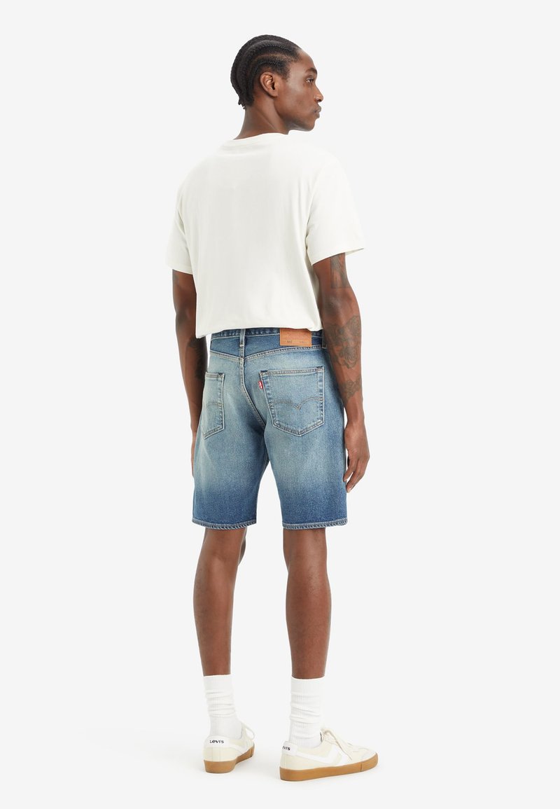 Jeans-Shorts mit einer hellblauen Wäsche, geradem Schnitt und umgeschlagenen Saum. Kombiniert mit einem weißen T-Shirt und weißen Socken mit Sneakers.