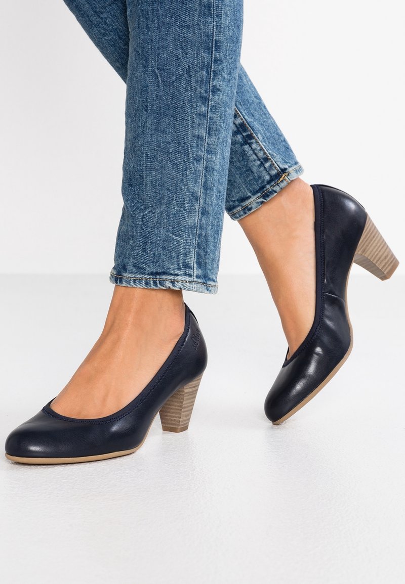 Chaussures à talons hauts en cuir bleu marine avec un bout arrondi et un talon en bois texturé couleur tan, assorties à un jean slim à chevilles.