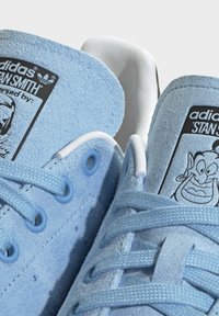 Ljusblå mockaskor med vita snören, med en svart tunga-label som har tecknade bilder och små, runda ögla.