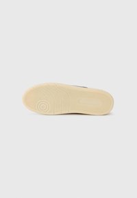 Semelle de chaussure présentant un design texturé avec un motif en zigzag, en matériau en caoutchouc beige clair, et accent avec un logo rond près du talon.