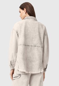 Szara kurtka dżinsowa z luźnym krojem, postrzępionym dołem i guzikami przy mankietach. Materiał ma miękką teksturę z delikatnym wykończeniem w stylu vintage.