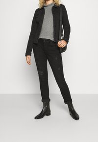 Czarna dżinsowa kurtka na szarym golfie, w połączeniu z przetartymi czarnymi dżinsami i czarnymi botkami za kostkę. Posiada minimalistyczny design.