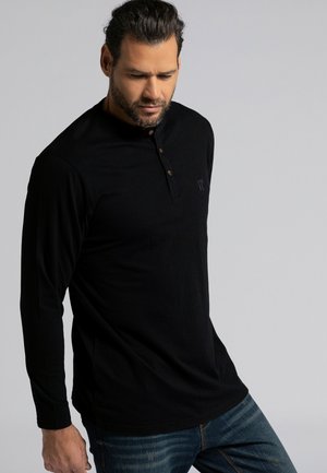 Camisa henley negra de manga larga con una tapeta de tres botones y un sutil detalle de logo. Fabricada con tejido suave y liso, presenta un corte relajado.