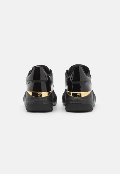 Baskets noires avec une finition brillante, un talon texturé et des accents dorés à l'arrière. Design bas avec des cols rembourrés pour plus de confort.