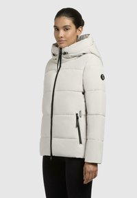 Giacca bianca imbottita con cappuccio, caratterizzata da zip e dettagli neri. Realizzata in materiale liscio, ha una forma squadrata e un design trapuntato.