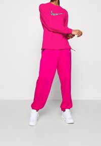Top de manga larga de Nike y pantalones a juego en rosa brillante; el top presenta un logo a rayas en blanco y negro; los pantalones tienen bolsillos laterales y puños elásticos.