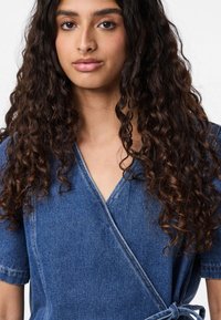 Abito avvolgente in denim con maniche corte, scollo a V e fascia in vita da legare. Tessuto blu medio texture con dettagli di cucitura visibili.