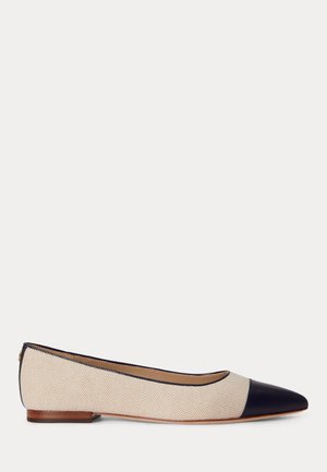 Zapato plano de mujer con tejido beige texturizado, punta de cuero negro en forma puntiaguda, tacón bajo de madera y ribete negro alrededor de la apertura.