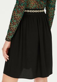 Czarna spódnica z marszczonym wzorem, zestawiona z dekoracyjnym paskiem łańcuszkowym. Przezroczysta, wzorzysta bluzka z zielonymi i brązowymi rękawami w zwierzęcy wzór.