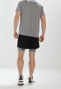 Idrottskläder bestående av en grå kortärmad skjorta, svarta shorts och ljusgrå kompressionsshorts. Skorna är svarta och vita med en sportig design.