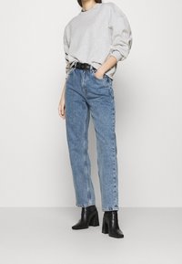 Felpa oversize grigia chiara con scollatura rotonda abbinata a jeans blu a vita alta e gamba dritta, oltre a stivali neri con tacco spesso.