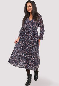 Vestido midi azul marino con flores, mangas largas, diseño cruzado, cintura con cinturón y tejido transparente; presenta pequeños patrones de flores rosas y blancas.