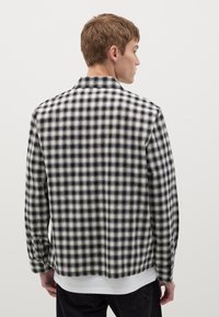 Chemise à carreaux noir et blanc en tissu doux, dotée d'un col classique, de manches longues et d'une coupe droite.