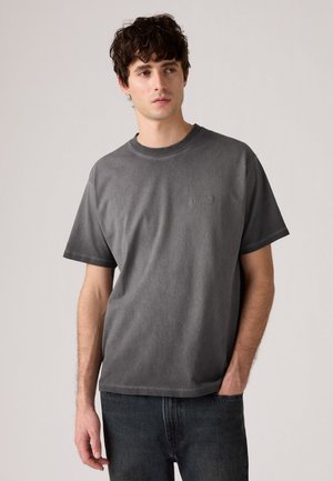 Gray cotton t-shirt with short sleeves, a round neckline, and a small embroidered logo on the chest, paired with dark denim jeans.