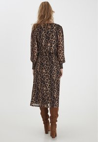 Šaty s leopardím vzorem s vykrojeným pasem, dlouhými rukávy a splývavým střihem. Průhledná tkanina v zemitých tónech s tmavými akcenty.