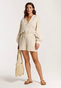 Helebeežist linast kleiti, sügava V-kaelusega ja õhuliste varrukatega, vöökoha peal kitsendatud ning sobivate lühikestega. Varustatud kootud kotiga.