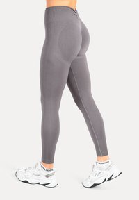 Leggings gris taille haute avec une coupe ajustée et une texture respirante. Dotés de coutures plates et de détails subtils le long des côtés.