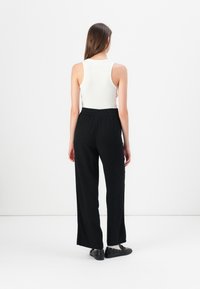 White ribbed tank top paired with loose, black pants. The pants feature an elastic waistband and fall to the ankles. Black shoes complete the outfit.