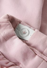 Détail en tissu rose avec un bandeau élastique blanc mettant en avant un bouton transparent, montrant une couture et une texture douce.