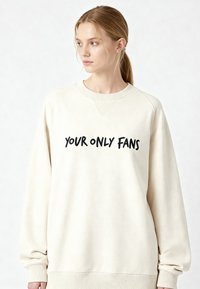 Felpa color crema con scollo rotondo, maniche raglan e testo nero con la scritta "YOUR ONLY FANS" sul davanti. Tessuto morbido.