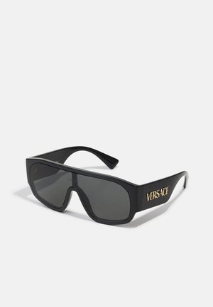 Óculos de sol oversized pretos com lentes escuras, armação larga e letras douradas "Versace" na lateral. Design elegante e contemporâneo.