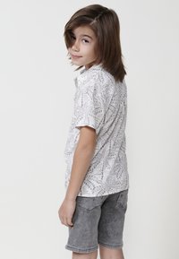 Balta trumpa rankovėmis marškiniai su pilku lapelių raštu, derinami su pilkais džinsiniais šortais. Yra klasikine apykakle ir laisva išvaizda.