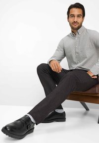 Dunkelgraue maßgeschneiderte Hose kombiniert mit einem hellgrauen karierten Hemd und schwarzen Slippern. Wolle-ähnliche Textur, Button-Down-Kragen und Fronttaschen-Detail.