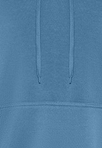 Sudadera azul con una textura suave, que cuenta con un bolsillo tipo canguro y cordones ajustables. Diseño sencillo, sin patrones ni acentos.