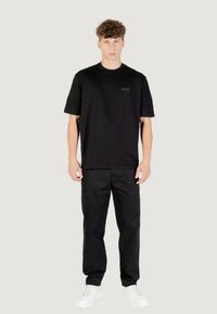 Camiseta negra de manga corta con un discreto logo en el pecho, combinada con pantalones cargo negros y zapatillas blancas, todo con un diseño simple y moderno.