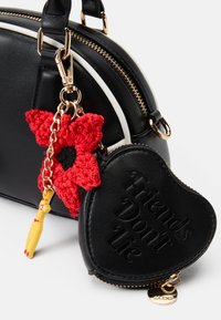 Borsa in pelle nera con accenti bianchi, caratterizzata da un ciondolo a forma di fiore all'uncinetto rosso e un portachiavi a forma di cuore con l'etichetta "Gli amici non mentono."