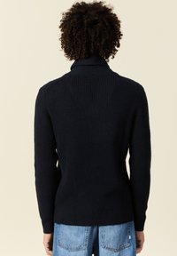 Maglione lavorato a maglia blu navy con colletto alto, motivo testurizzato e maniche lunghe, rifinito con polsi e orlo a coste.