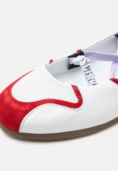 Chaussure plate blanche et rouge avec détail en daim à l'avant et bride élastique violette ornée de lettres blanches en relief.