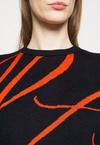 Knit sweater in black with bold red abstract patterns. Features a crew neck and textured fabric with visible stitch details.
