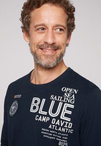 Camicia a maniche lunghe blu navy in cotone, con testo e loghi stampati in bianco, design con colletto rotondo e vestibilità rilassata.