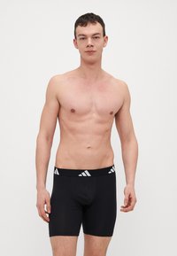 Fekete boxer alsónadrág elasztikus anyagból, széles derékpánttal, fehér csíkokkal, és sima felülettel.