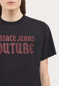 T-shirt in cotone nero con lettering in rhinestone rosso audace. Collo rotondo e maniche corte. Etichetta di cura visibile all'interno.