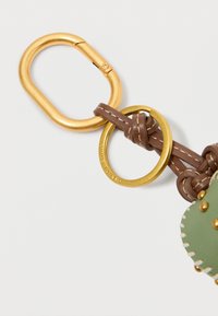 Roheline nahkaksessuaar tekstureeritud viimistlusega, millel on kuldne metallist karabiin ja pruunad nahktükid, sealhulgas dekoratiivne õmblus.