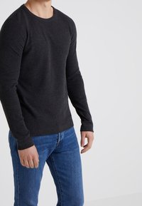 Långärmad, lättstickad tröja i mörkgrått med rund halsringning och ribbade muddar, kombinerad med blå jeans.