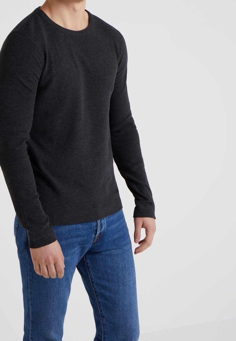 Långärmad, lättstickad tröja i mörkgrått med rund halsringning och ribbade muddar, kombinerad med blå jeans.