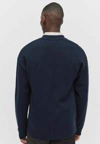 Mörkblå stickad tröja med ribbad fåll och ärmslut. Har en klassisk rund halsringning och helärmar, designad för en avslappnad passform.